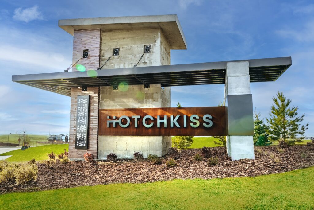 Modern entrance sign for the Hotchkiss community, featuring large metal letters mounted on a concrete and brick structure with landscaping in the foreground.